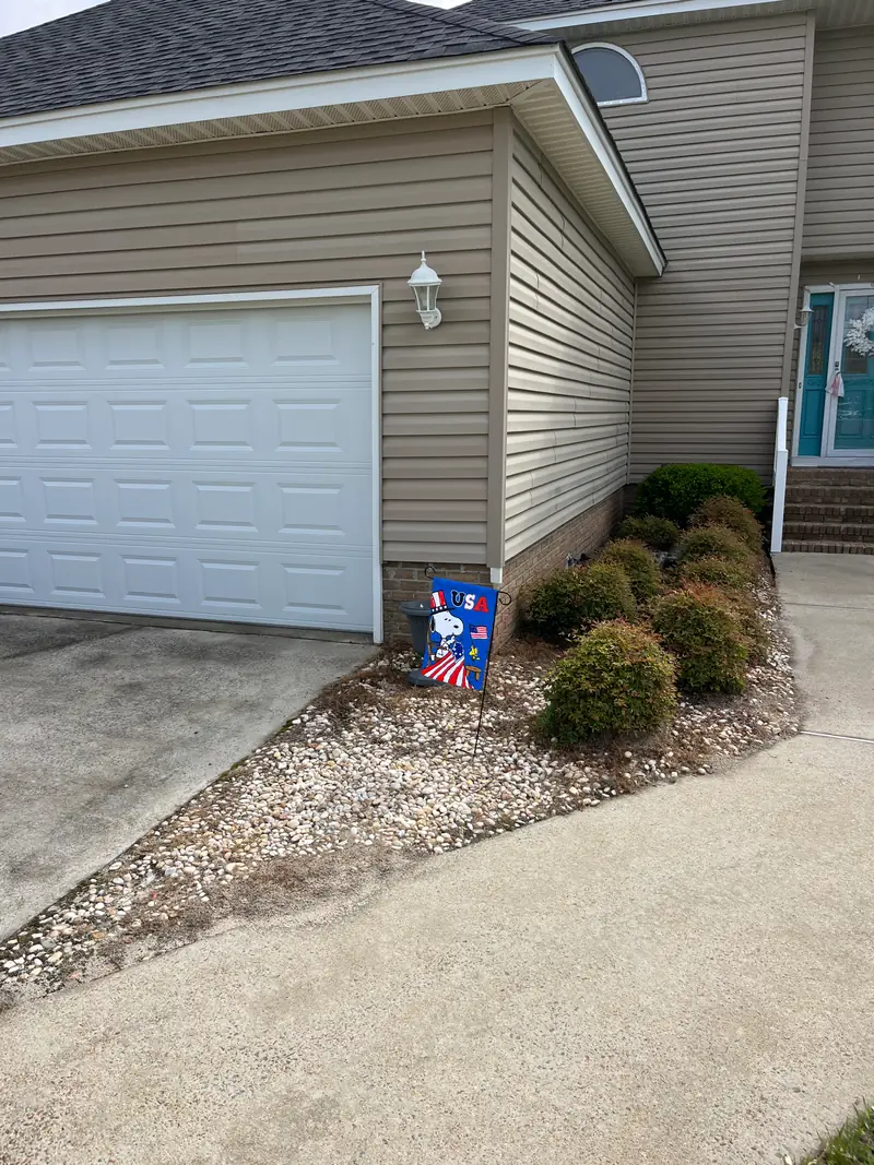 River rock bed and clipped shrubs beside a garage