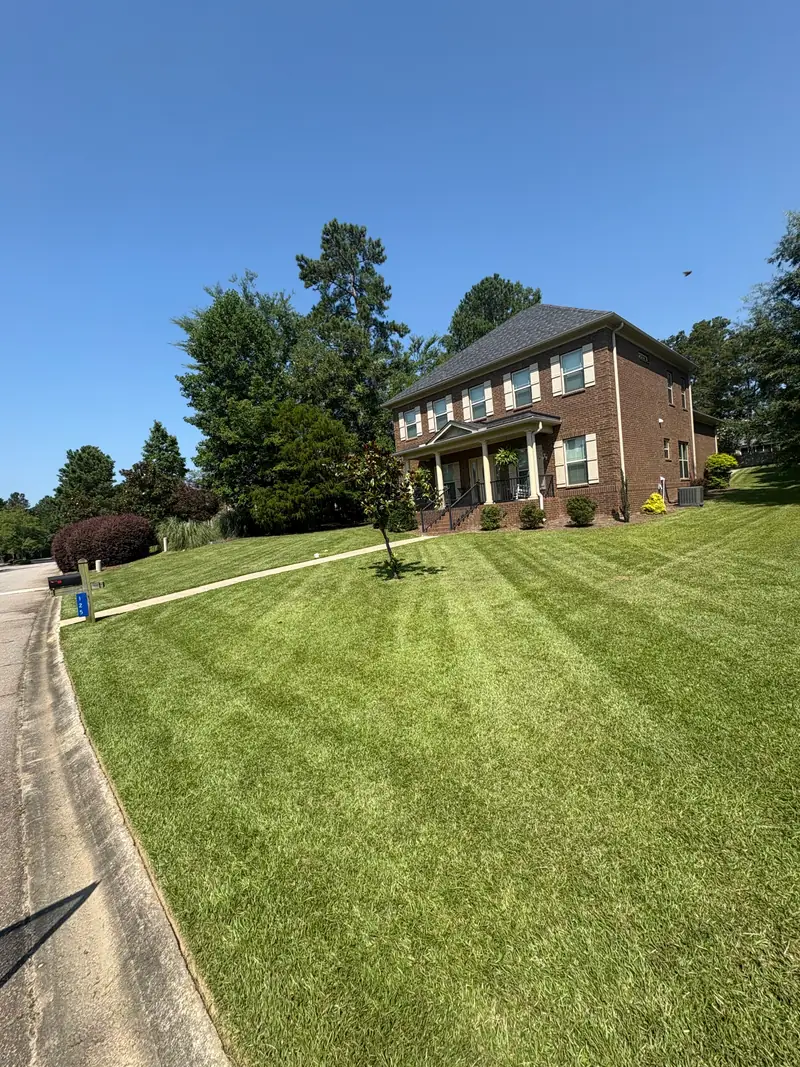 Striped mowing across the front lawn of a two-story brick home